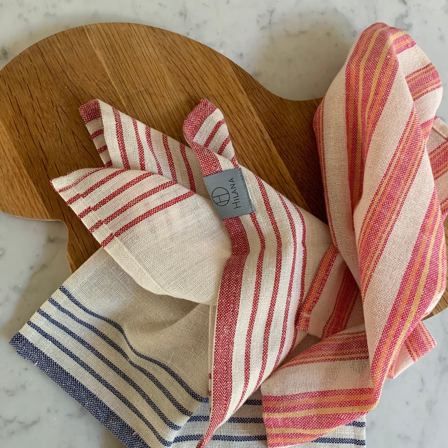 Striped linen tablecloth set in cream, magenta, and navy with woven texture on wooden surface