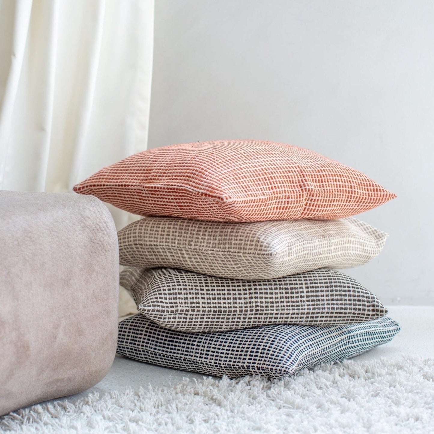 Woven throw pillow covers stacked in rust, beige, gray, and blue textured fabrics with minimalist geometric patterns