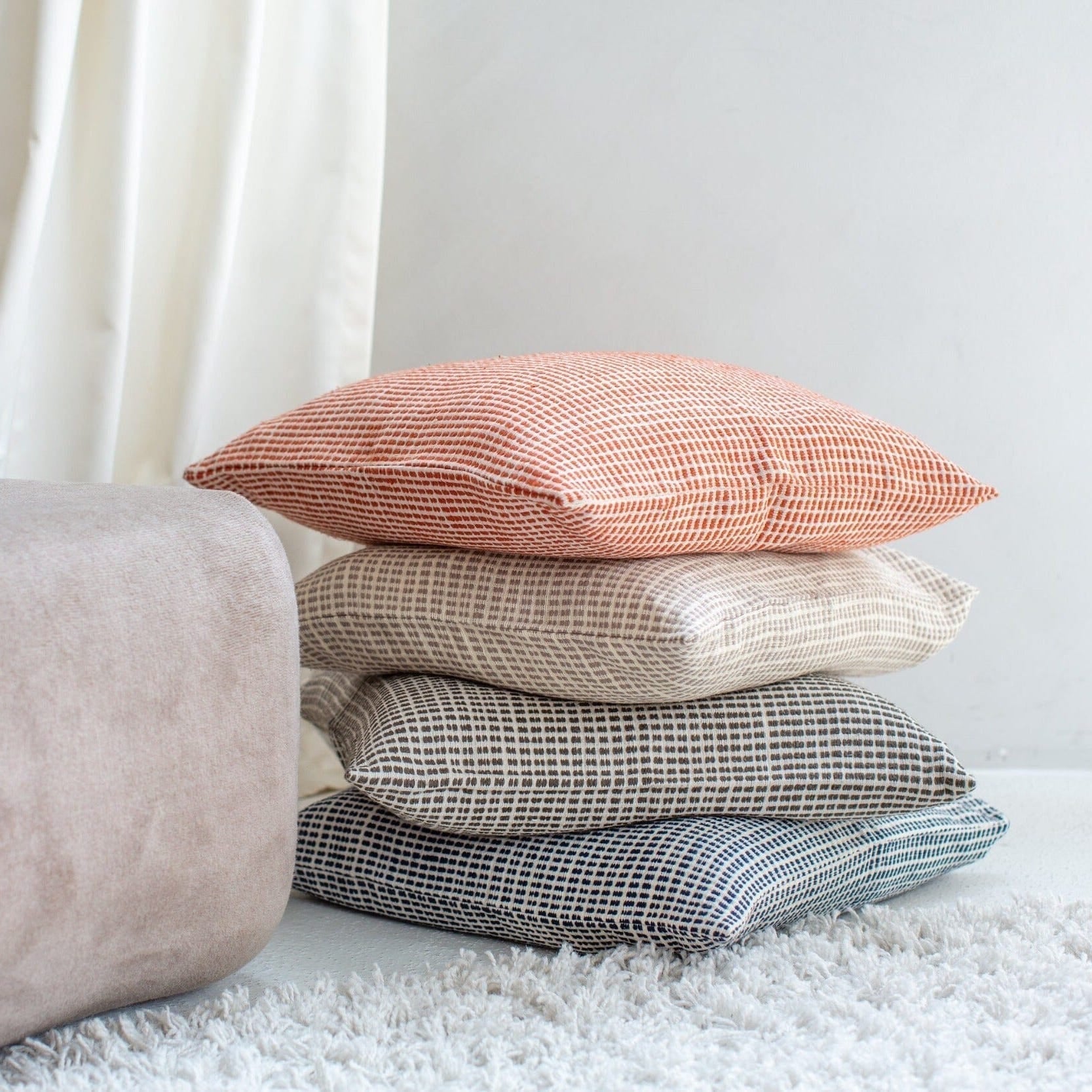 Woven throw pillow covers stacked in rust, beige, gray, and blue textured fabrics with minimalist geometric patterns