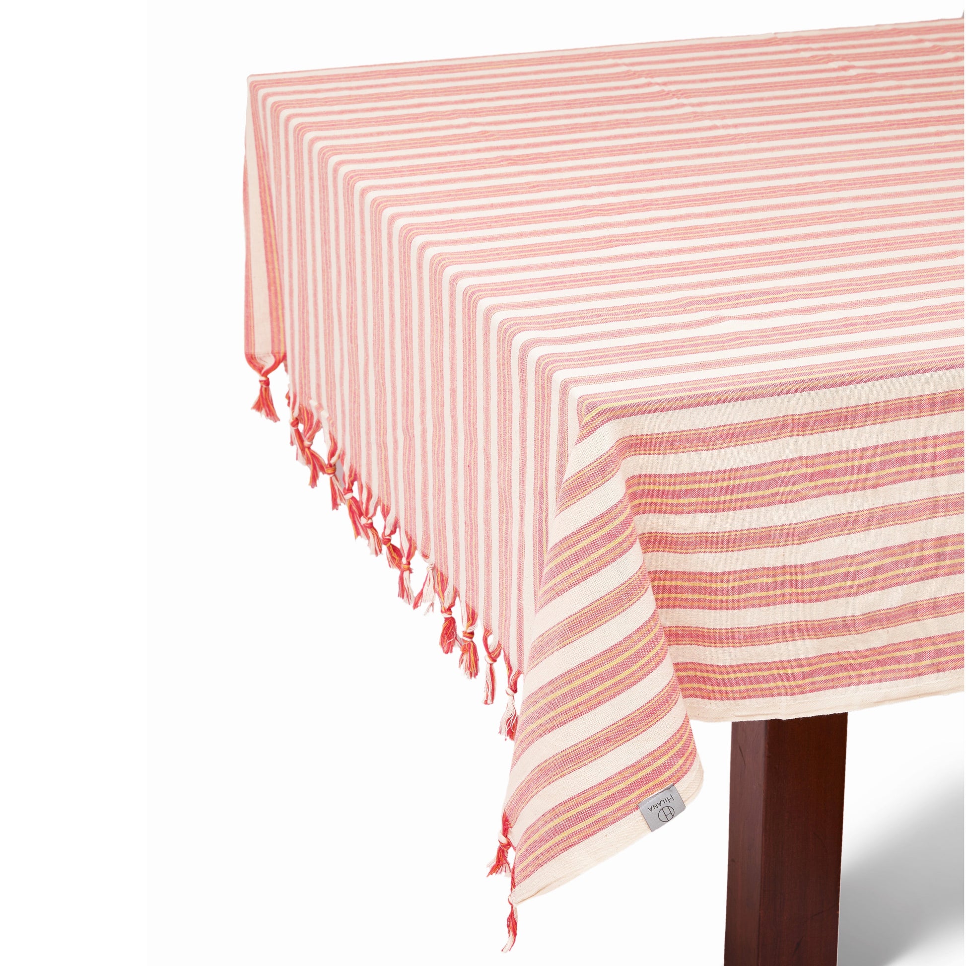 Coral and cream striped linen tablecloth with tassel edges draped on wooden table