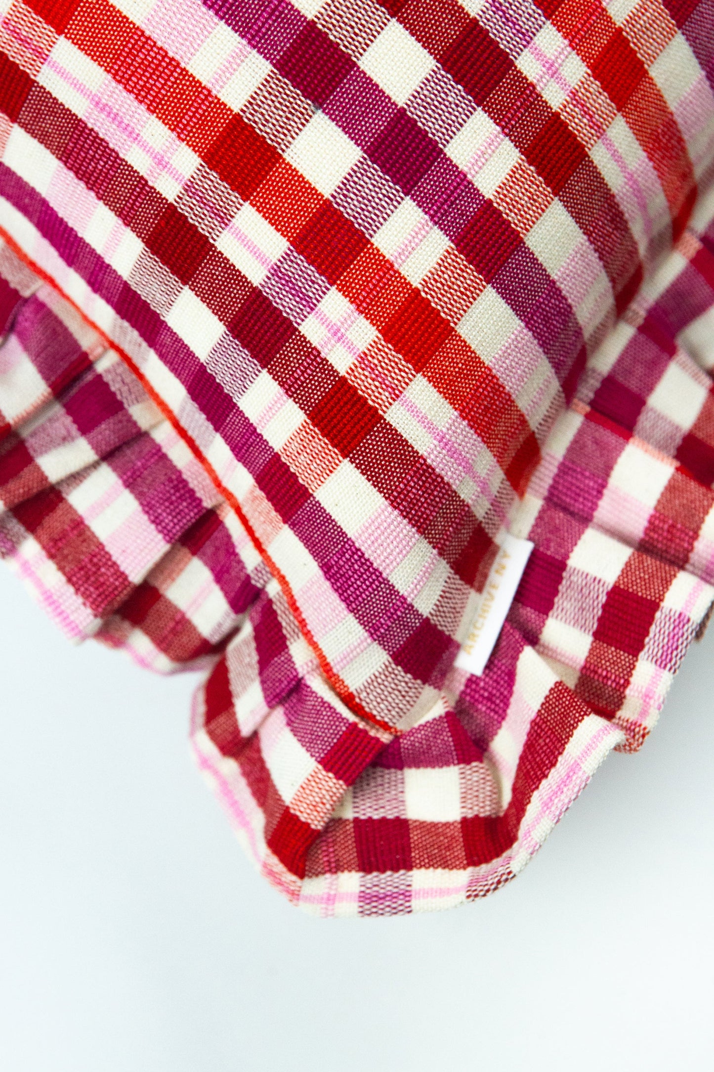 Red and magenta plaid throw pillow with cream stripes and textured weave fabric ruffle edge
