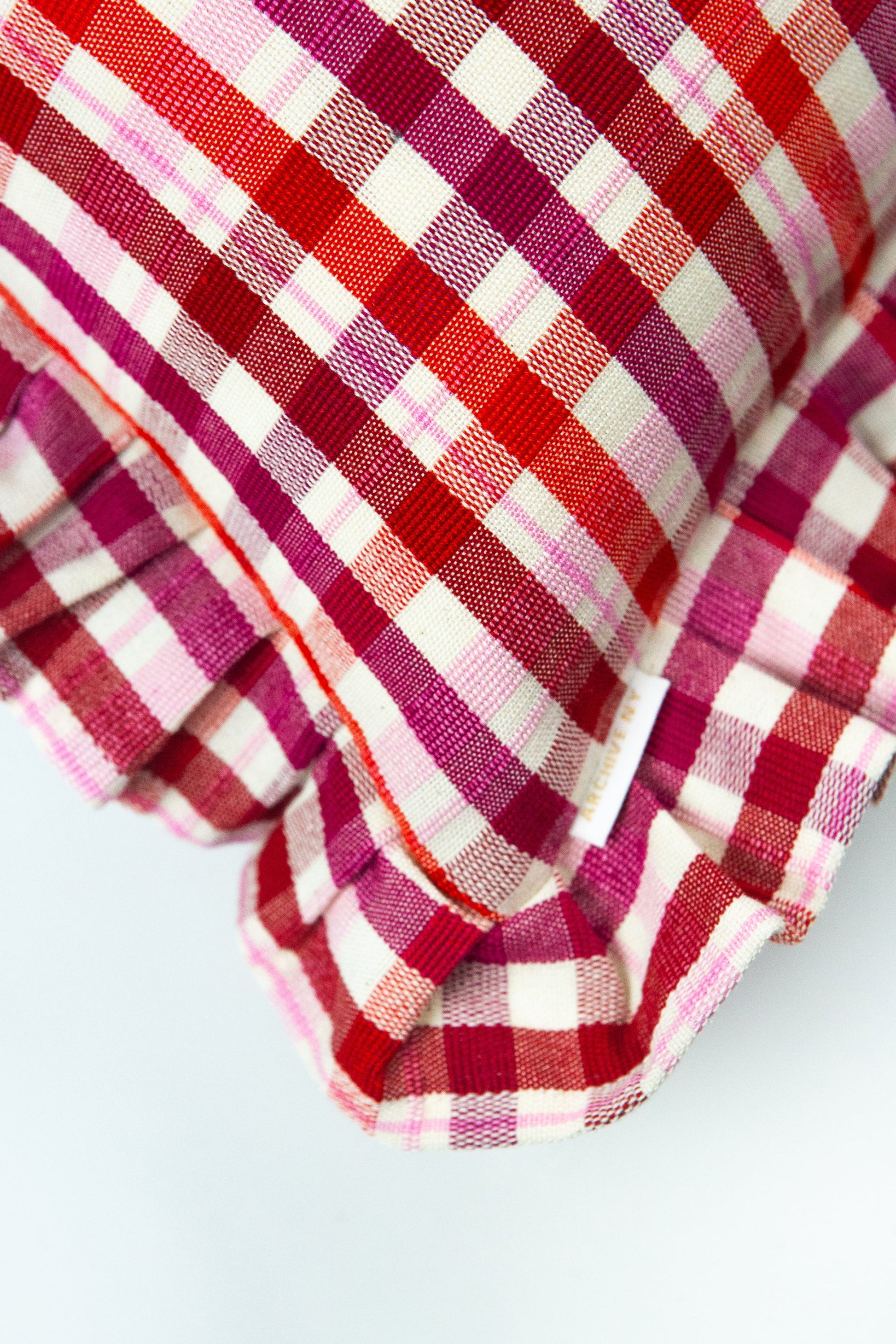 Red and magenta plaid throw pillow with cream stripes and textured weave fabric ruffle edge