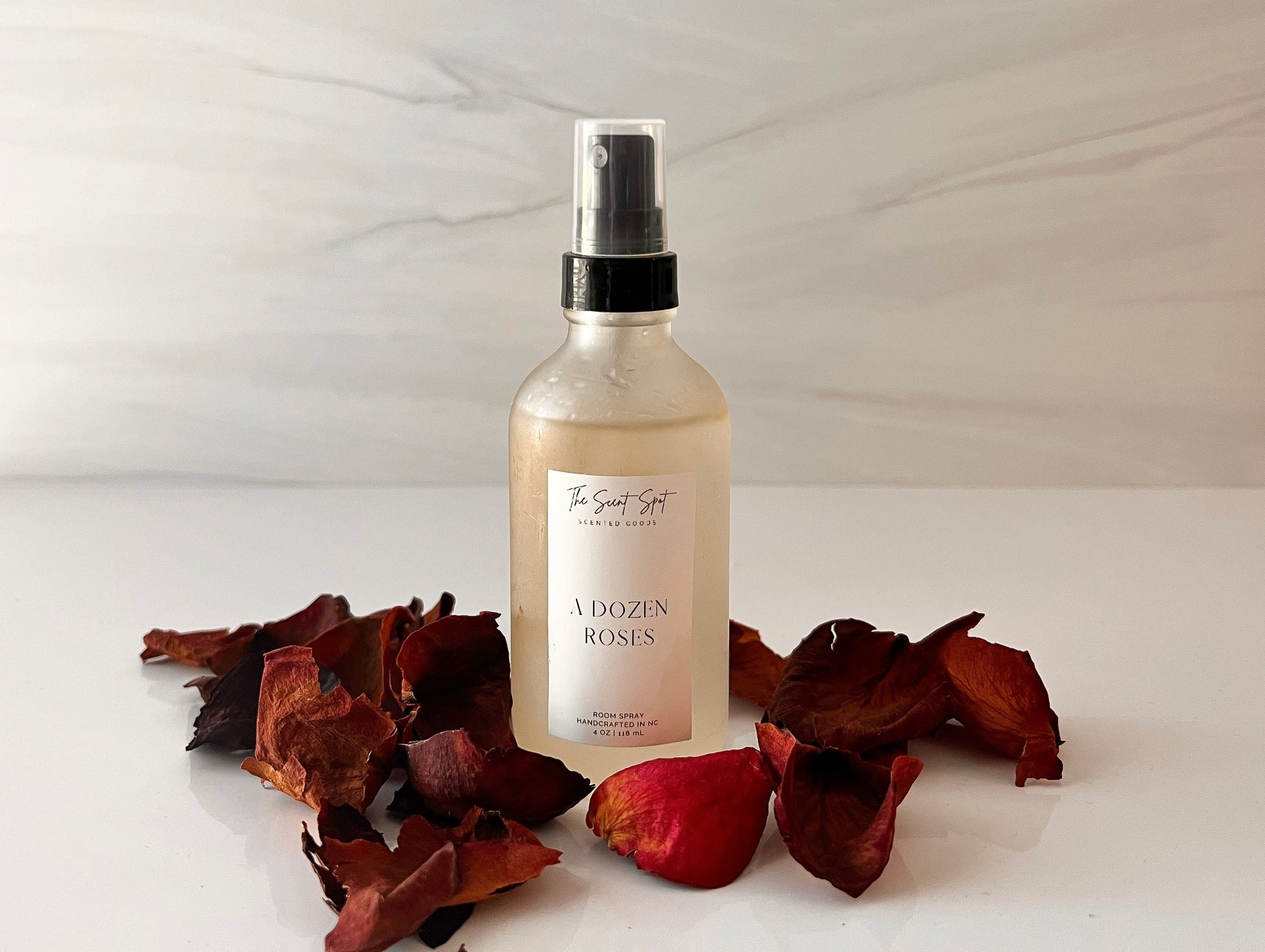 Rose room spray with black pump top, surrounded by dried red rose petals on marble surface