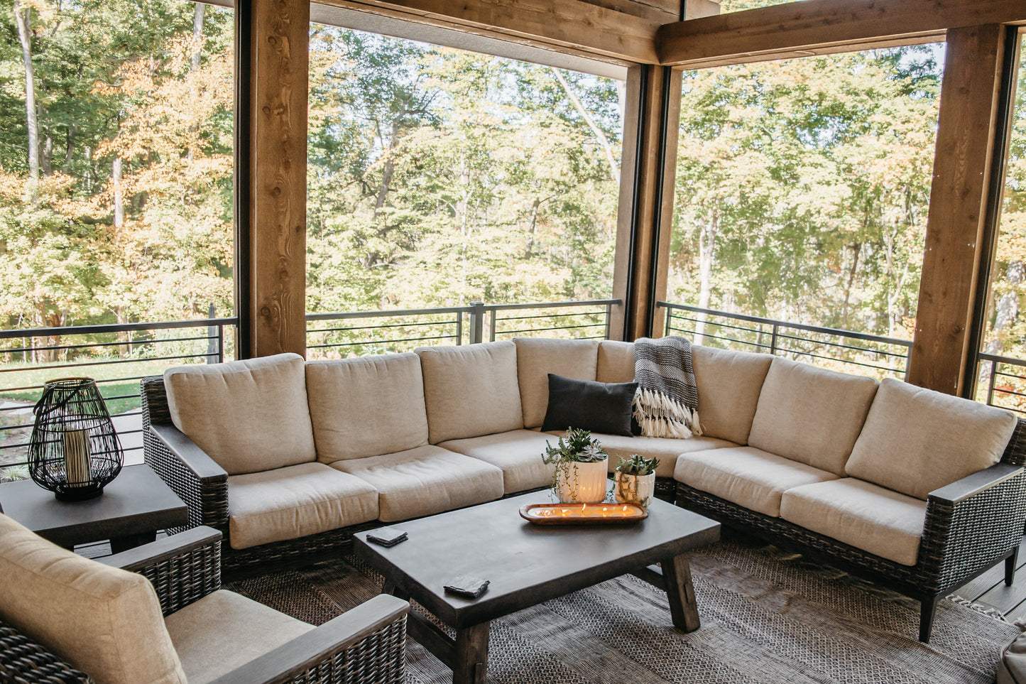 Woven rattan outdoor sectional with beige cushions and black coffee table on covered porch