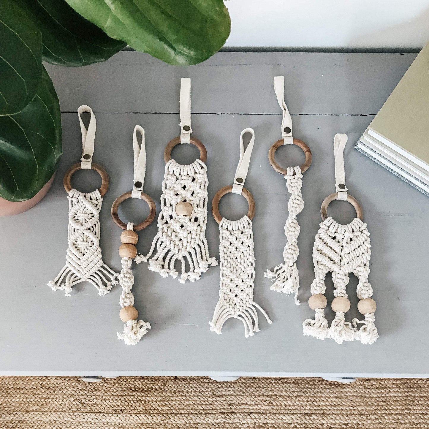 Macrame baby toy with wooden ring, cream cotton knotted fringe, and natural wood beads on white fabric loop