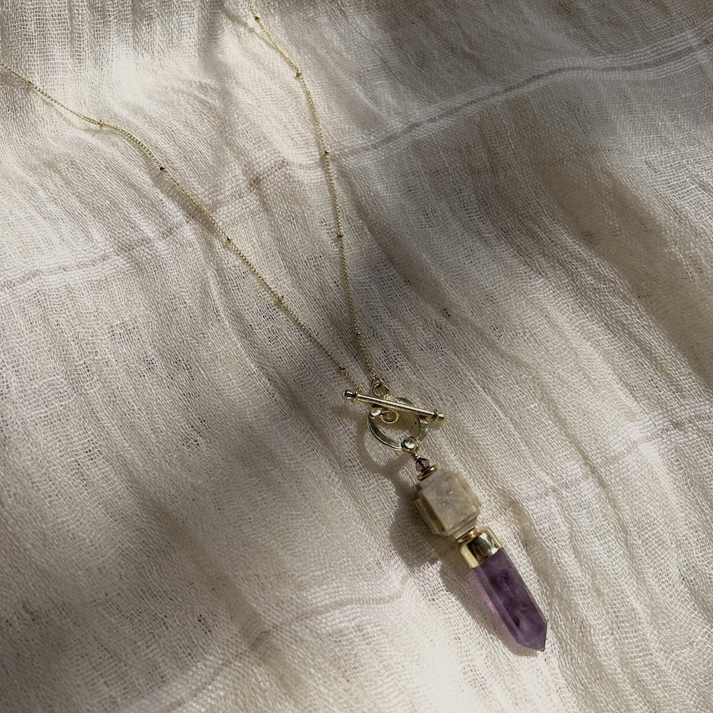 Gold lariat necklace with amethyst and white stone pendant on natural linen fabric