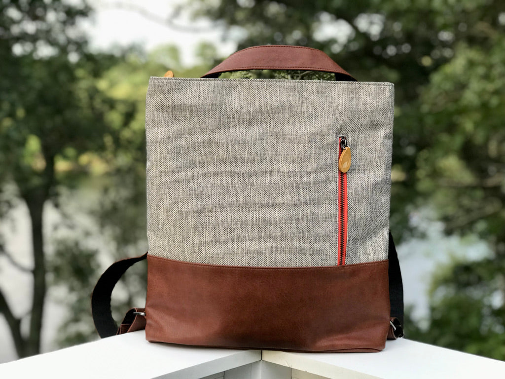 Beige linen and brown leather convertible backpack tote with red zipper detail and wooden button accent