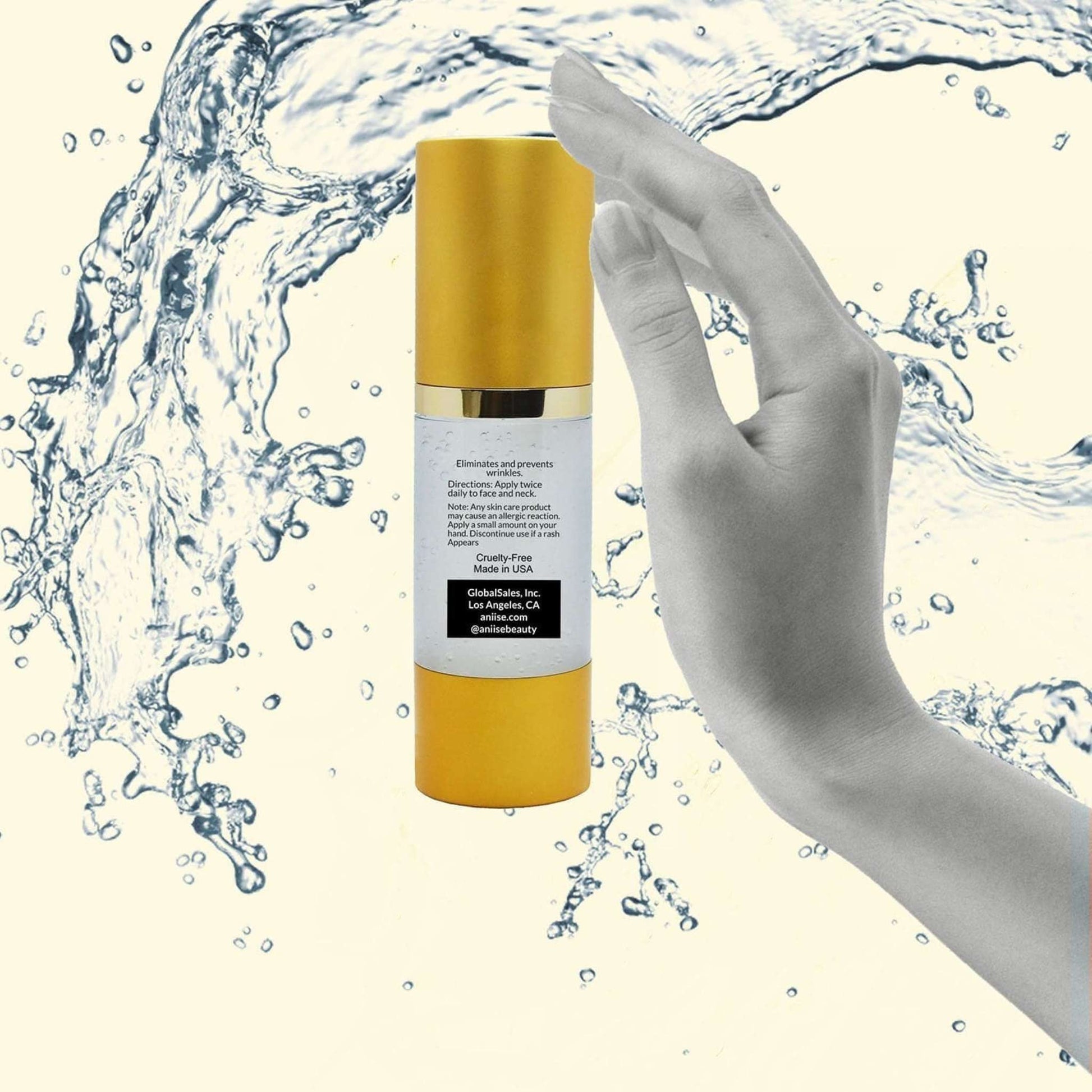 Gold and white cylindrical anti-aging serum bottle with gold cap held in hand surrounded by water splashes