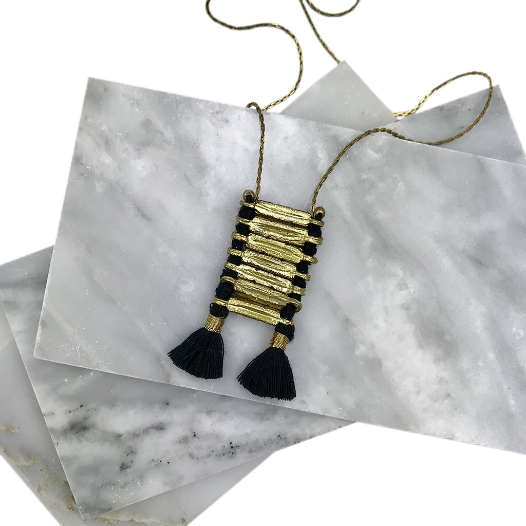 Gold-wrapped black tassel necklace pendant with brass cord on white marble background