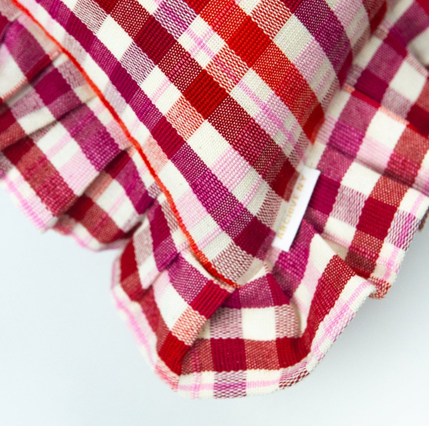 Red and magenta plaid pillow with ruffle edges and woven cotton texture in traditional gingham pattern