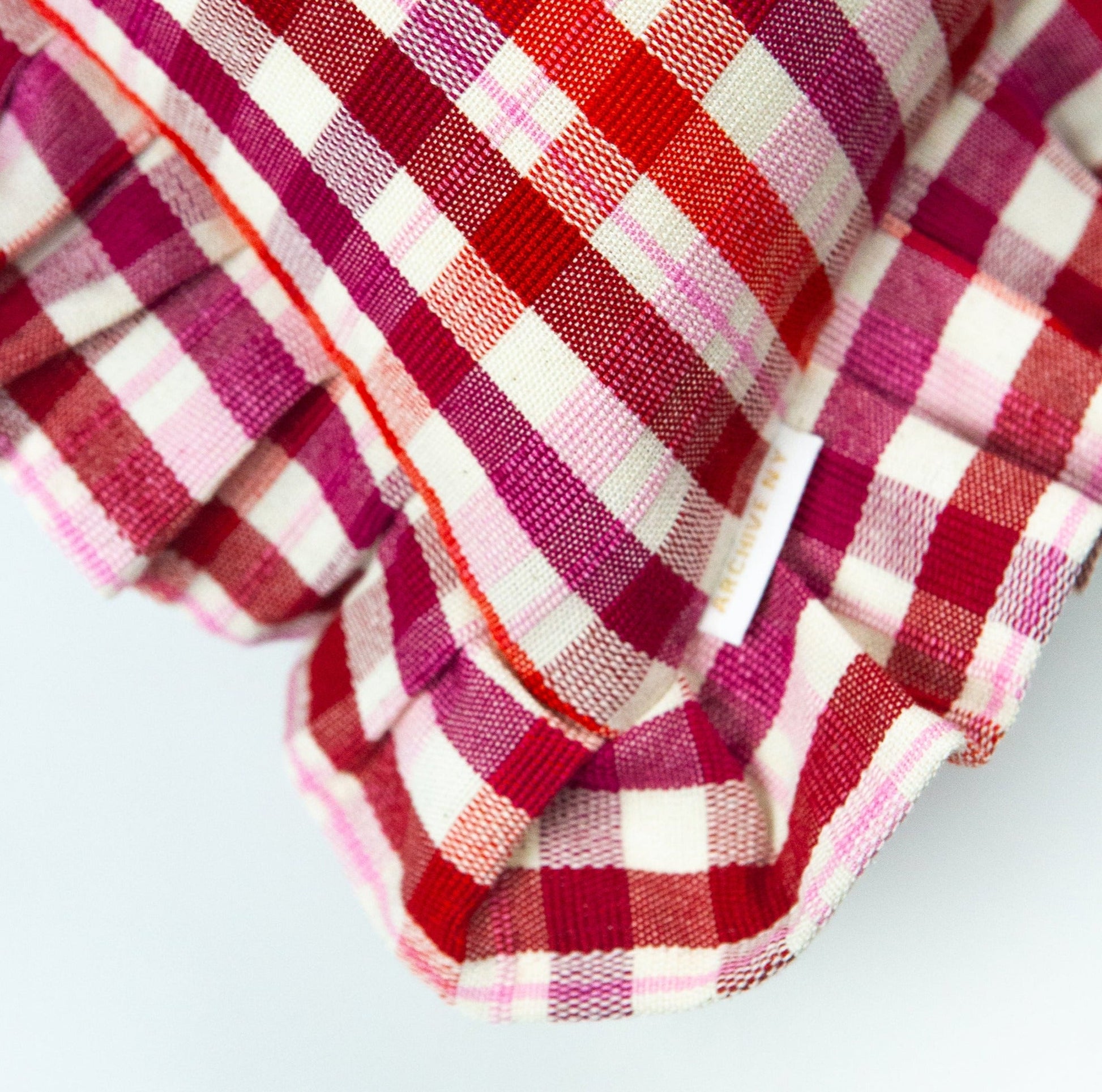 Red and magenta plaid pillow with ruffle edges and woven cotton texture in traditional gingham pattern