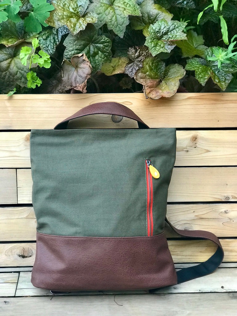 Sage canvas and burgundy leather convertible backpack with red zipper detail on wooden deck