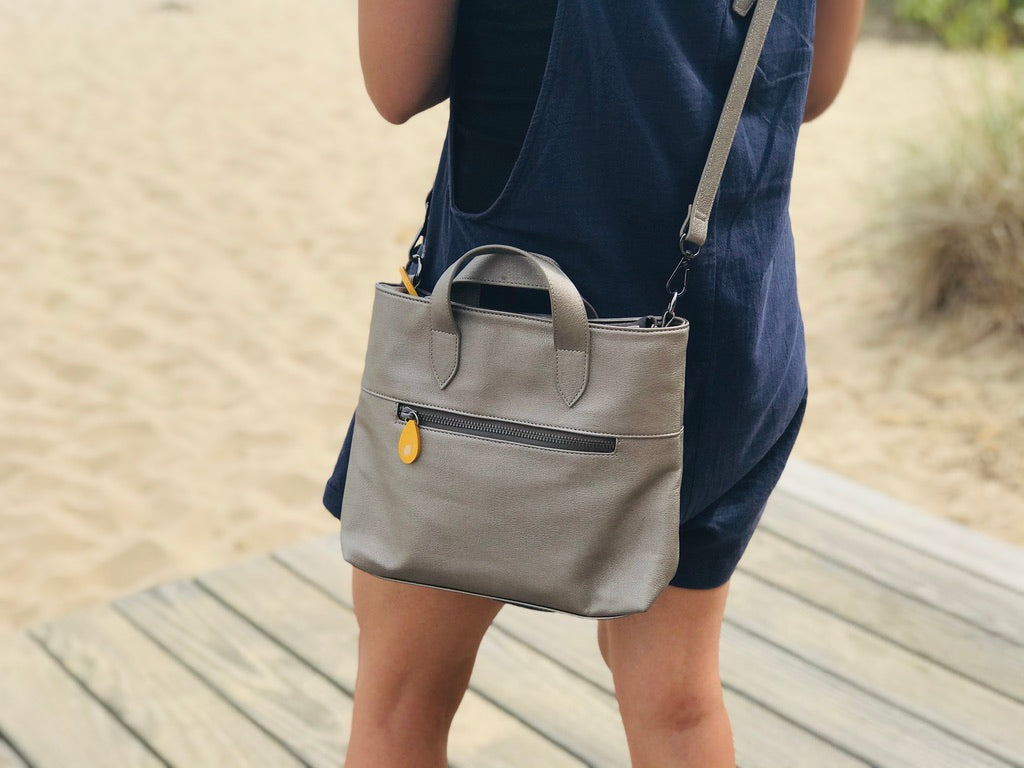 Beige canvas crossbody satchel with dual handles, adjustable strap, and front zip pocket with yellow accent