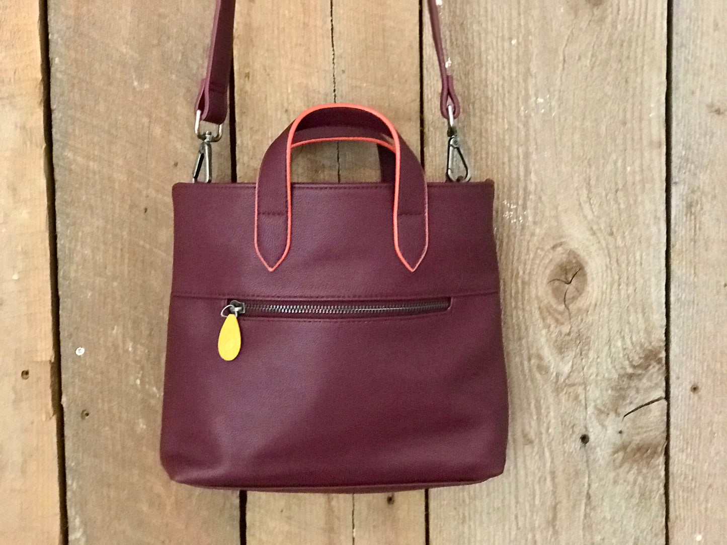 Burgundy leather crossbody satchel with coral-trimmed handles and yellow zipper accent, sustainable bag