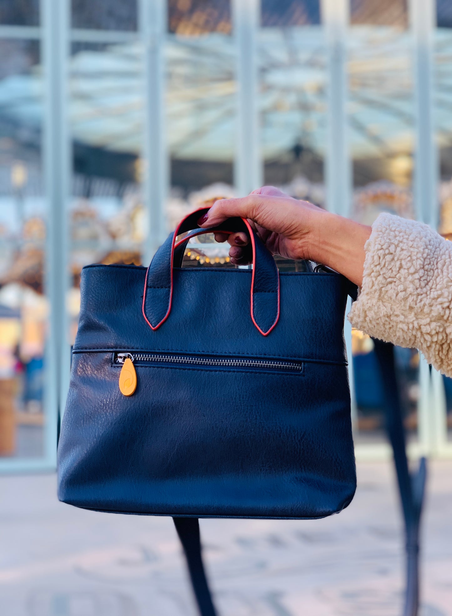 Navy leather satchel bag with red handles, yellow accent detail, and front zipper pocket for daily essentials