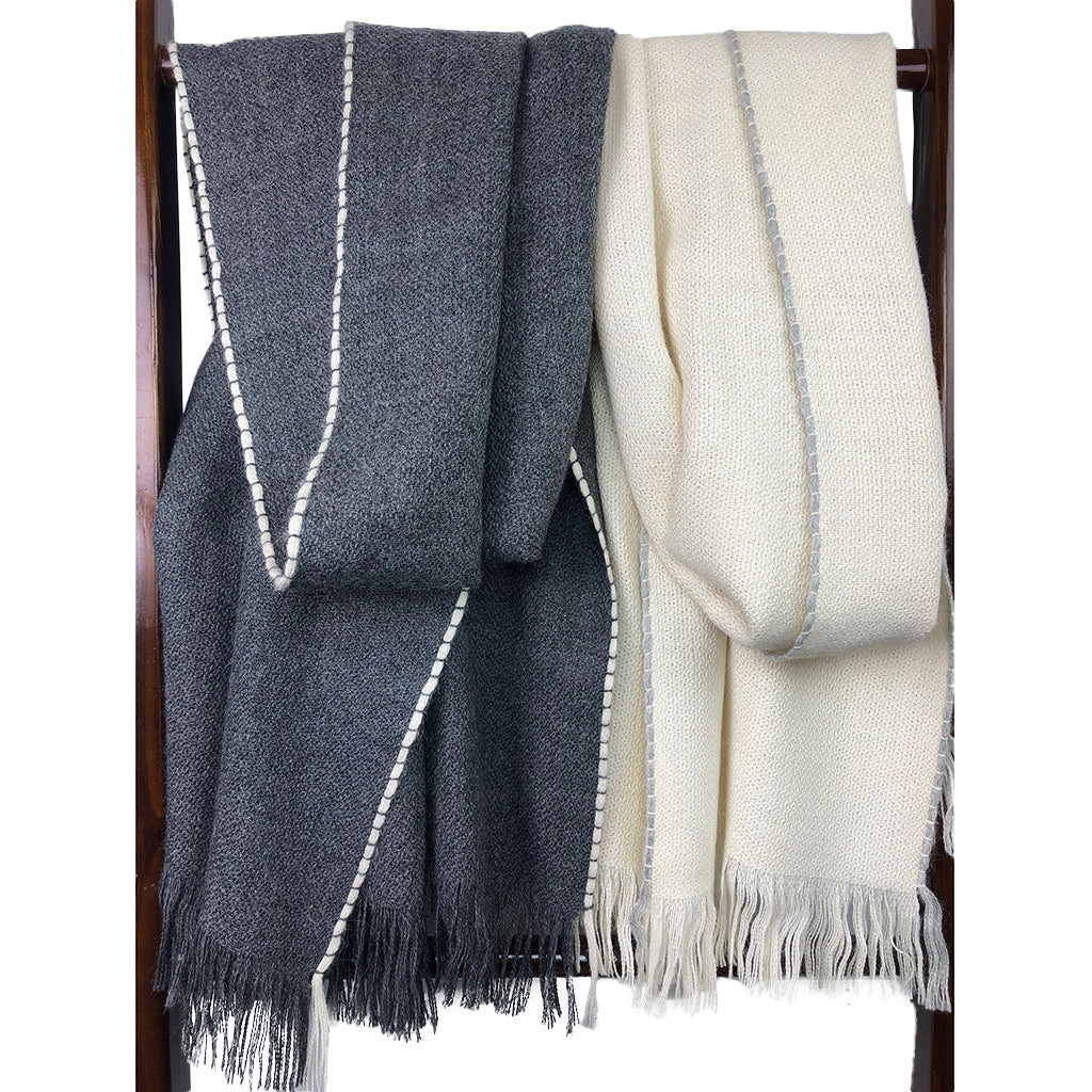 Charcoal and cream baby alpaca scarves with contrast stitching and fringe trim on wooden rack