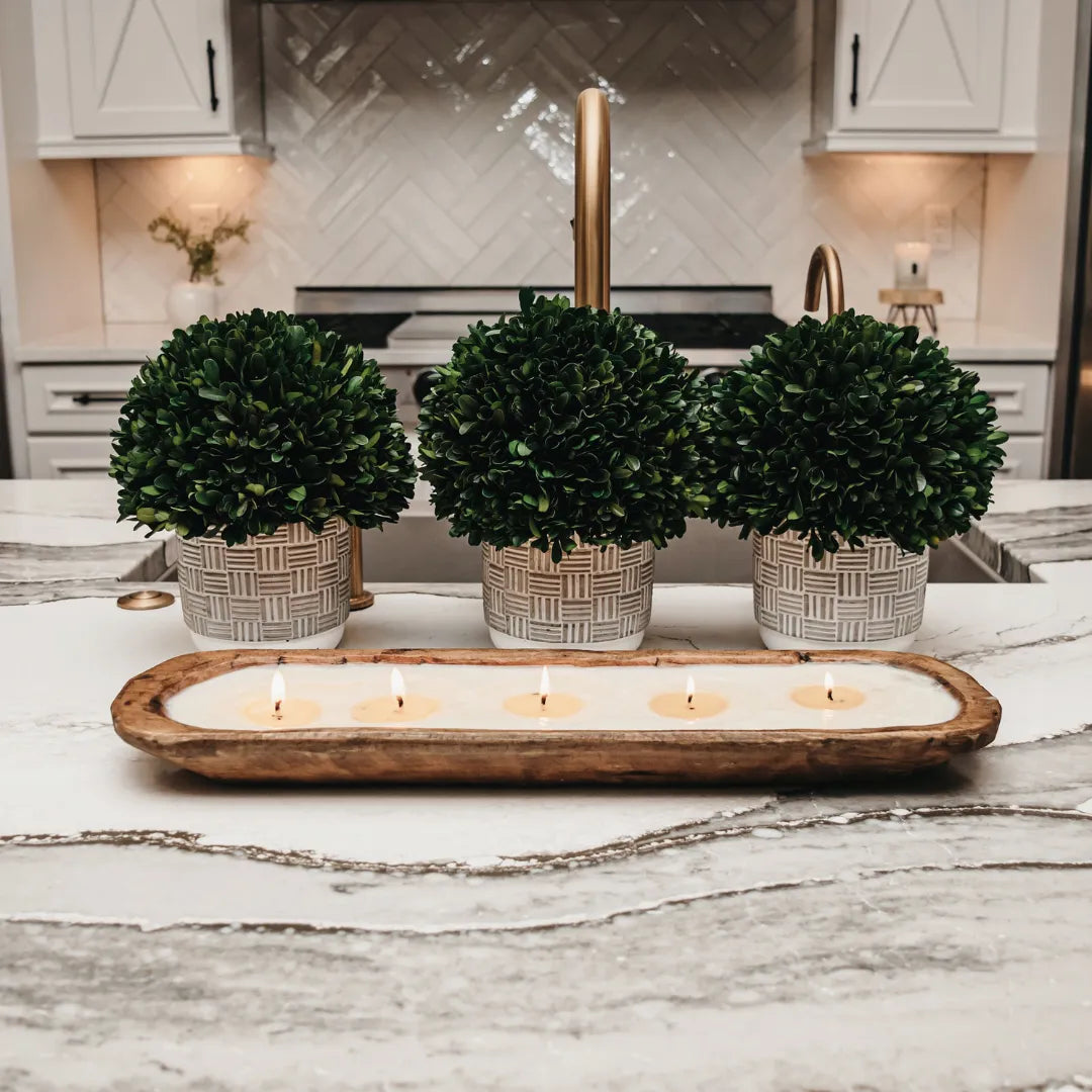 Five-wick soy candle in wood dough bowl with green boxwood topiaries in woven natural planters