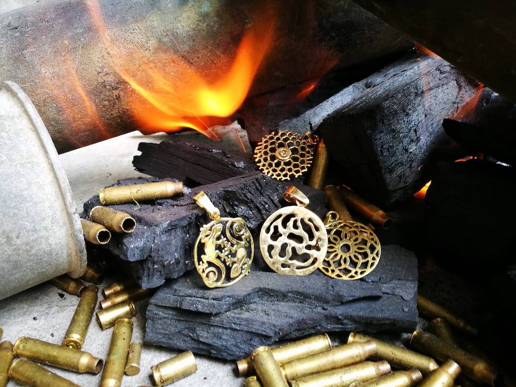 Brass bullet casing cuff bracelet with ornate filigree design displayed on charcoal next to open flame