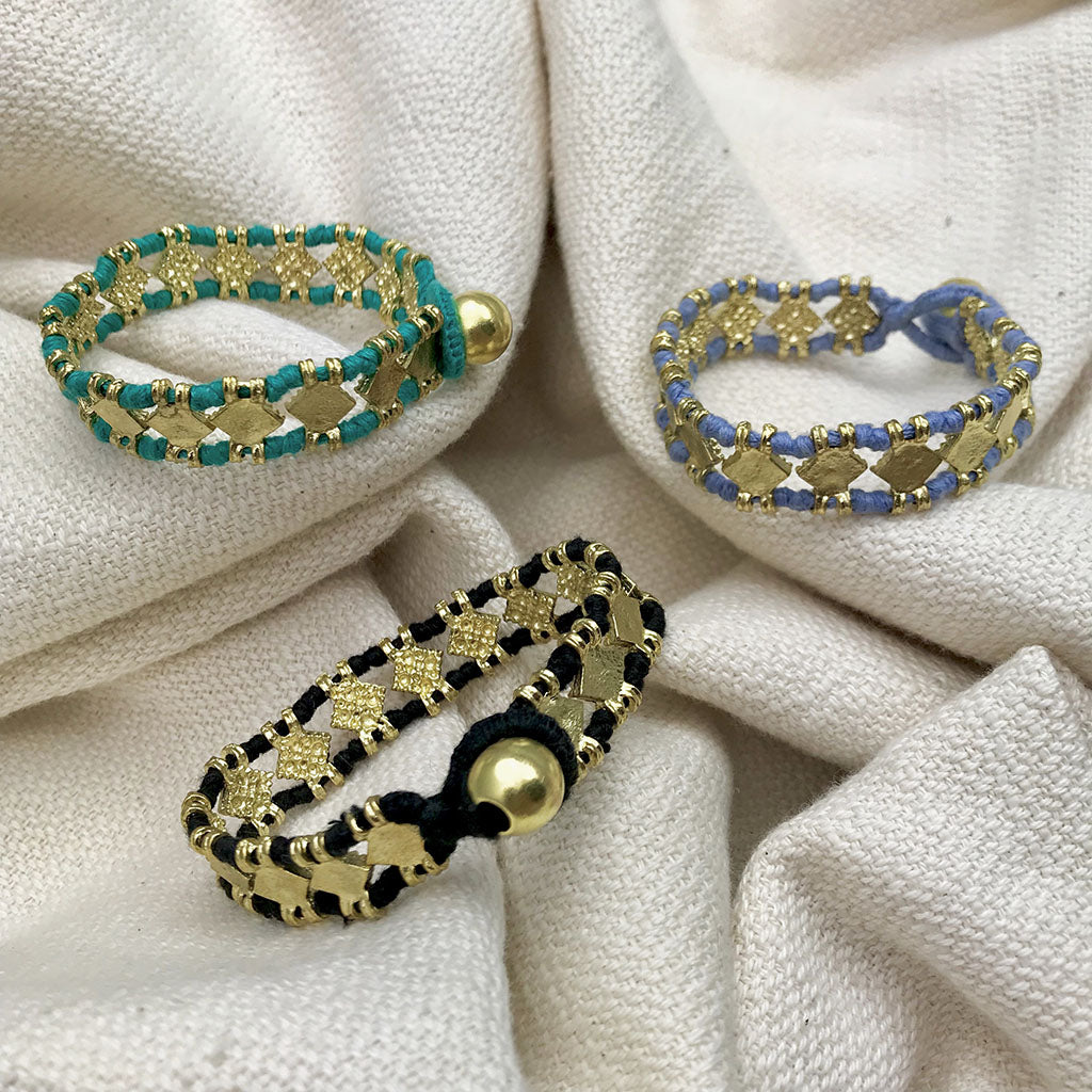 Beaded bracelets in teal, navy, and black with gold-tone metal accents and charm details on natural linen fabric